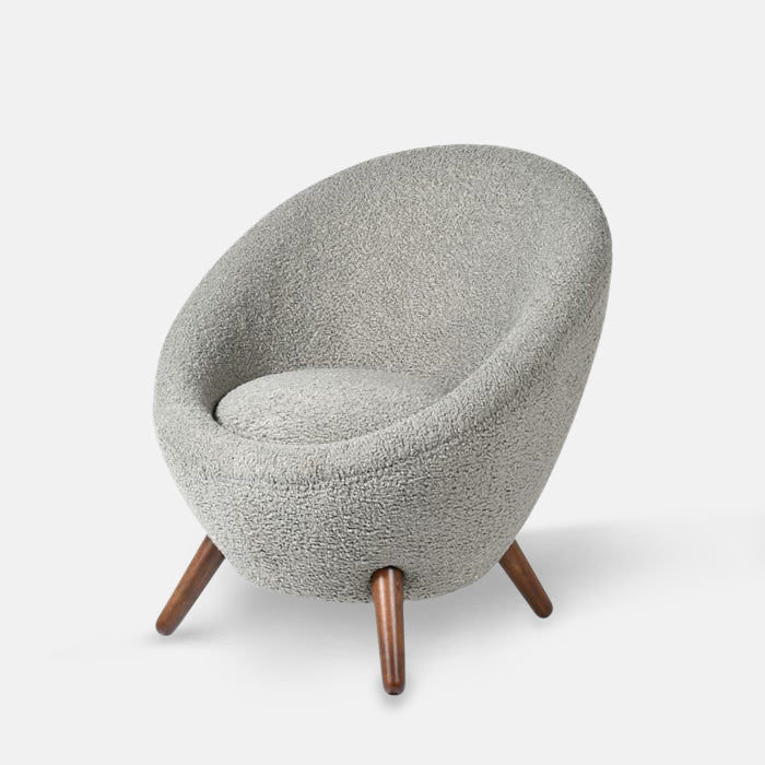 Armchair upholstered in grey boucle fabric with four short brown wooden legs.