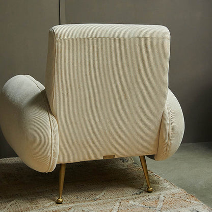 A large curvy cream armchair upholstered in a cream cord velvet fabric with gold metal legs.