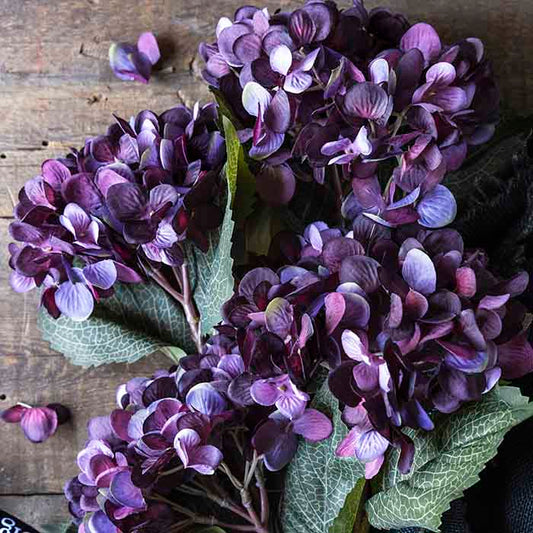 Artificial hydrangea flowers with deep purple blooms and green leaves.