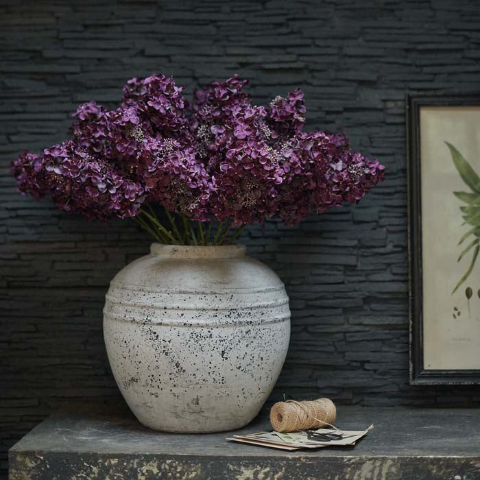 Large grey stoneware vase containing artificial hydrangea paniculata flowers in purple.
