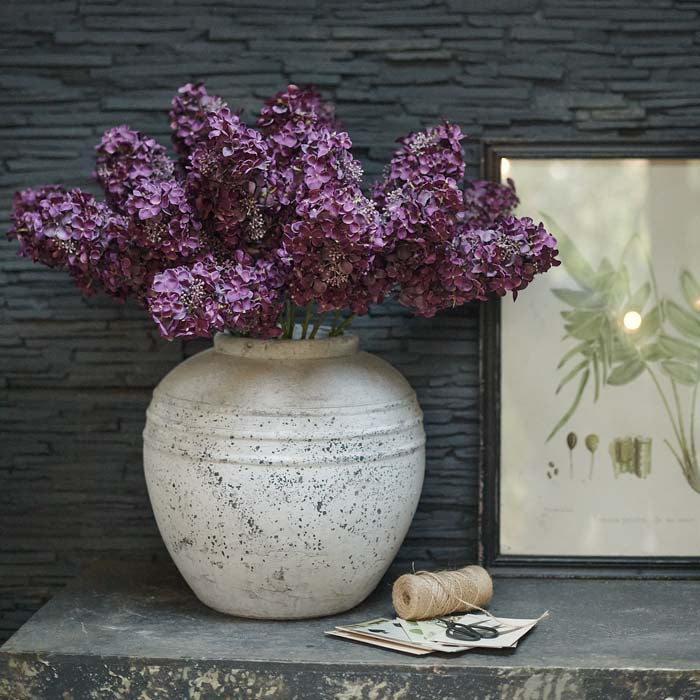 Artificial purple hydrangea paniculata flowers in a large grey stoneware vase.