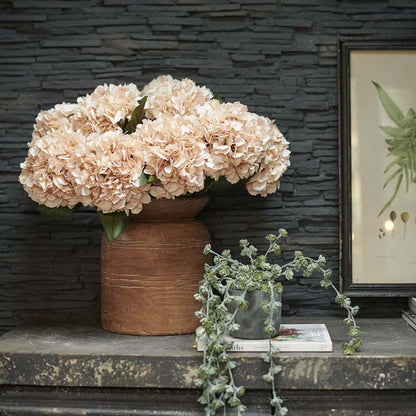 Large bunch of soft apricot faux hydrangea stems in a large brown vase
