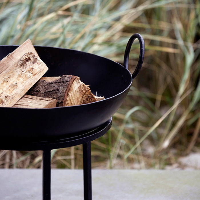 Round black metal fire pit with handles filled with wooden logs