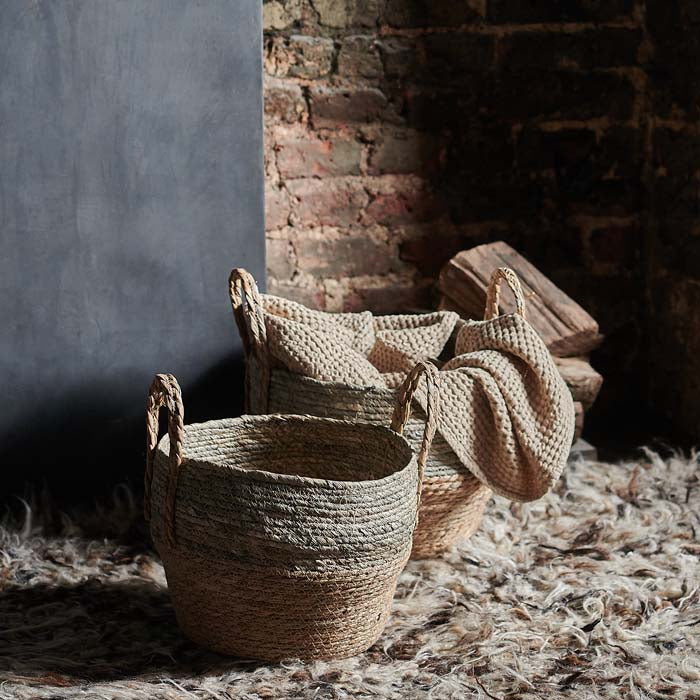Two brown and grey handled baskets sat on a brown shaggy rug in front of a fireplace
