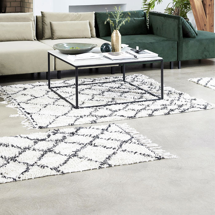 The Keoni Rug, a rectangular soft cream fringed rug with a black diamond design in a Berber style, in a lounge room.