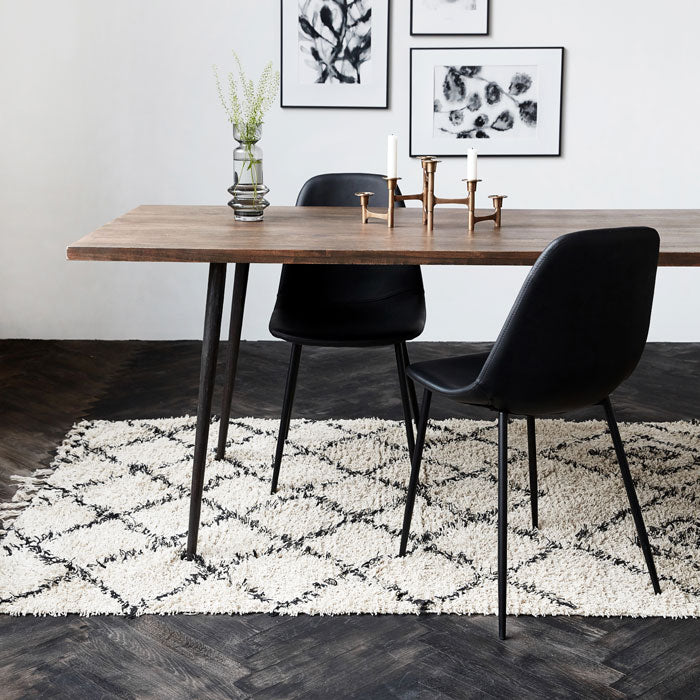 The Keoni Rug, a rectangular soft cream fringed rug with a black diamond design in a Berber style, in a lounge room.