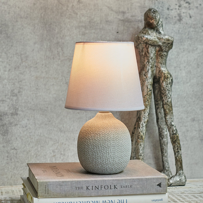 Round grey table lamp switched on in front of two hugging figurines
