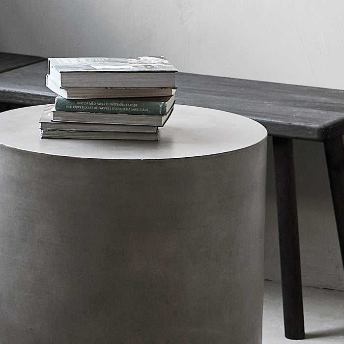 Round grey concrete side table with a stack of books on top