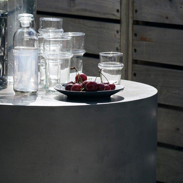 The Lander Side Table - Medium, a smooth cylindrical table made from grey concrete, with a bowl of cherries placed on top.