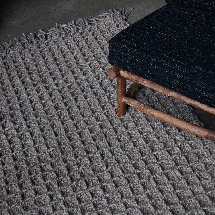 Raised small square patterned rug in brown under a wooden armchair