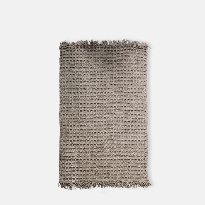 Large taupe grey-brown rug in waffle knit texture, with tasseled ends.