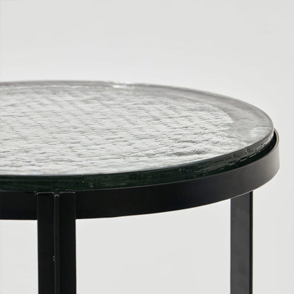 A round black metal side table with clear glass table top.