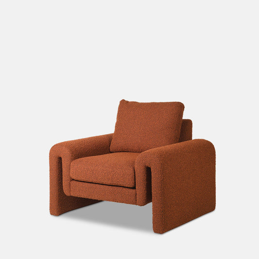 Large quirky shaped armchair with curved sides upholstered in terracotta boucle fabric.