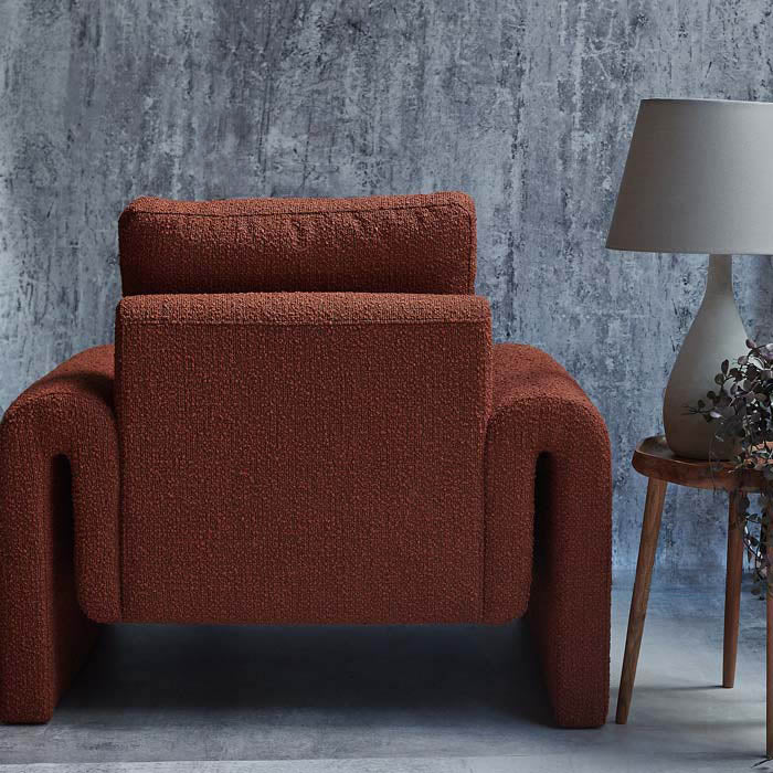 Large quirky shaped armchair with curved sides upholstered in terracotta boucle fabric.