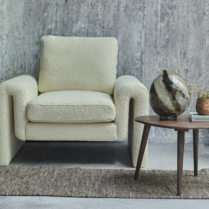 Large quirky shaped armchair with curved sides upholstered in cream boucle fabric.