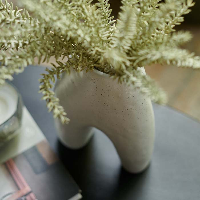 Green leafy stems placed in a glossy white ceramic vase sat on a black wooden table