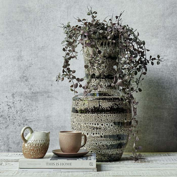 Matumbo Vase, a black and cream sculptural reactive glazed ceramic vase styled with some trailing purple stems.