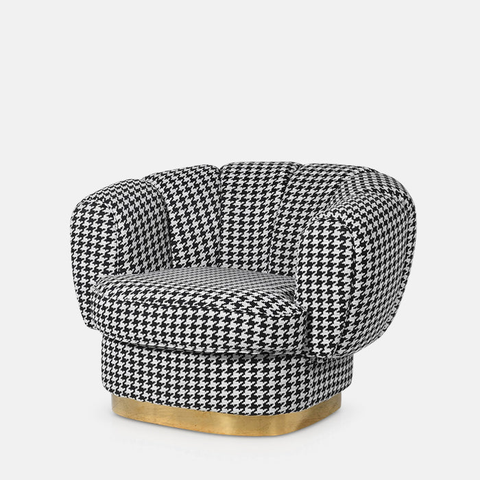 Large round armchair upholstered in black and white houndstooth fabric, sitting on gold metal platform base.