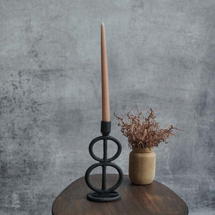 A sculptural aluminium candleholder in a matte black finish, with a pink tapered candle.