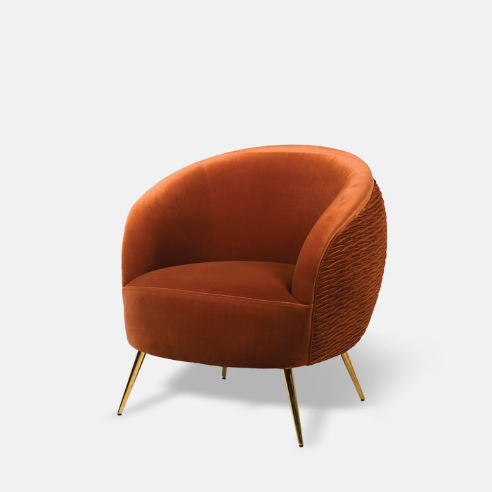 Curvy armchair with a textured back and upholstered in rust velvet fabric with gold metal legs.