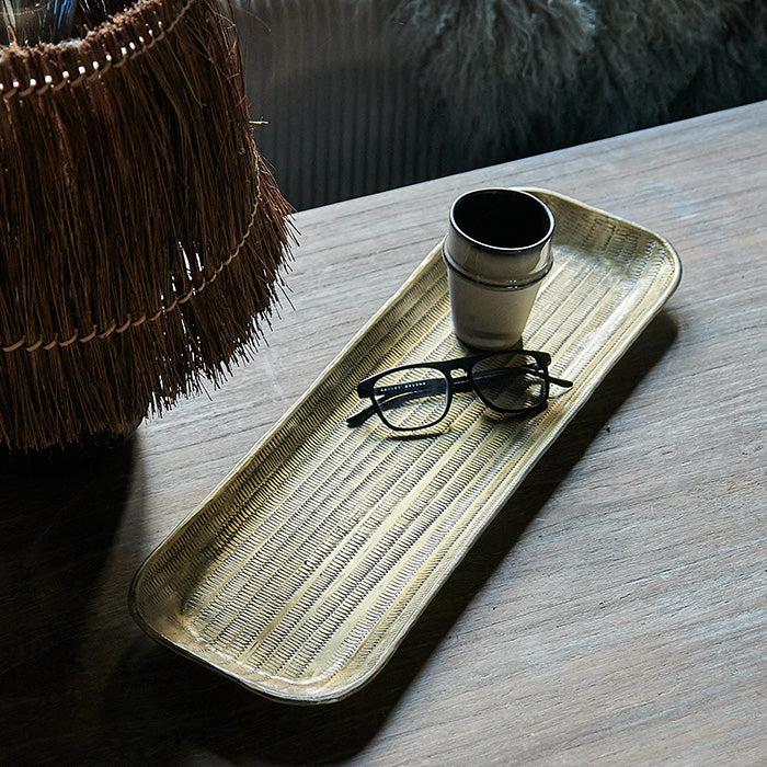 Rectangular hammered brass tray holding a ceramic mug and reading glasses.