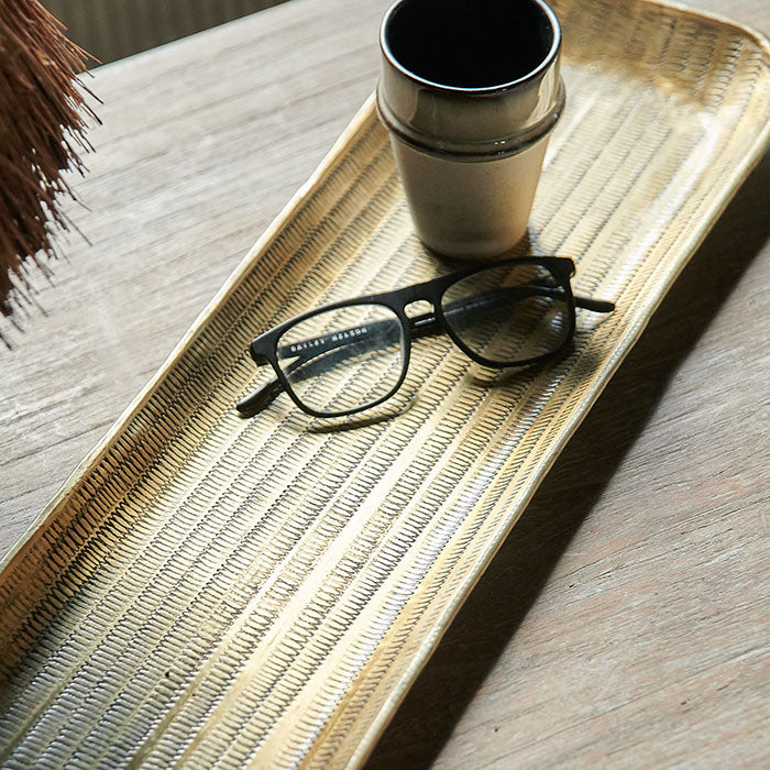 Reading glasses and ceramic mug on a hammered brass rectangular tray.