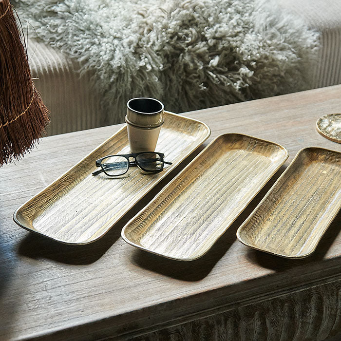 Three rectangular hammered brass trays, in different sizes, on a coffee table.