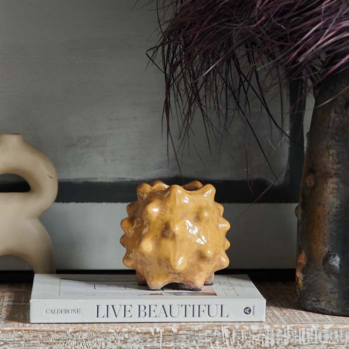 Otterley Stoneware Vase Honey, a small spiked textural vase in a warm honey coloured glossy glaze, sat on a book.