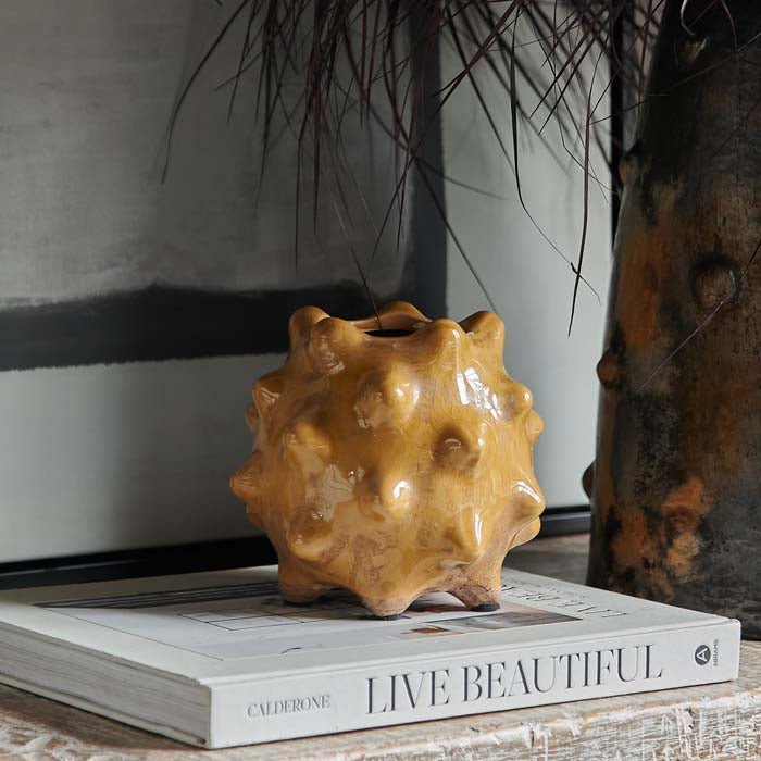 Otterley Stoneware Vase Honey, a small spiked textural vase in a warm honey coloured glossy glaze, sat on a book.