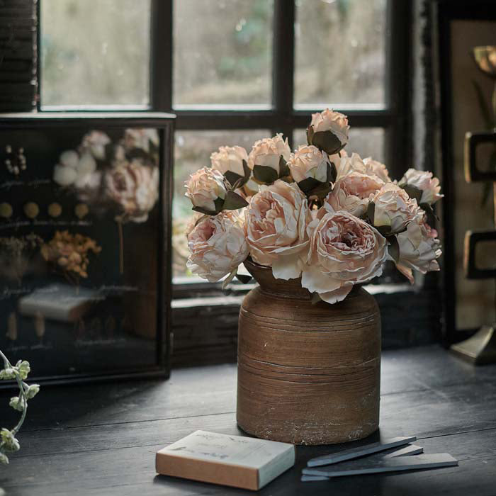 Wood-effect cement vase holding multiple stems of artificial peony flowers in a soft creamy blush tone.