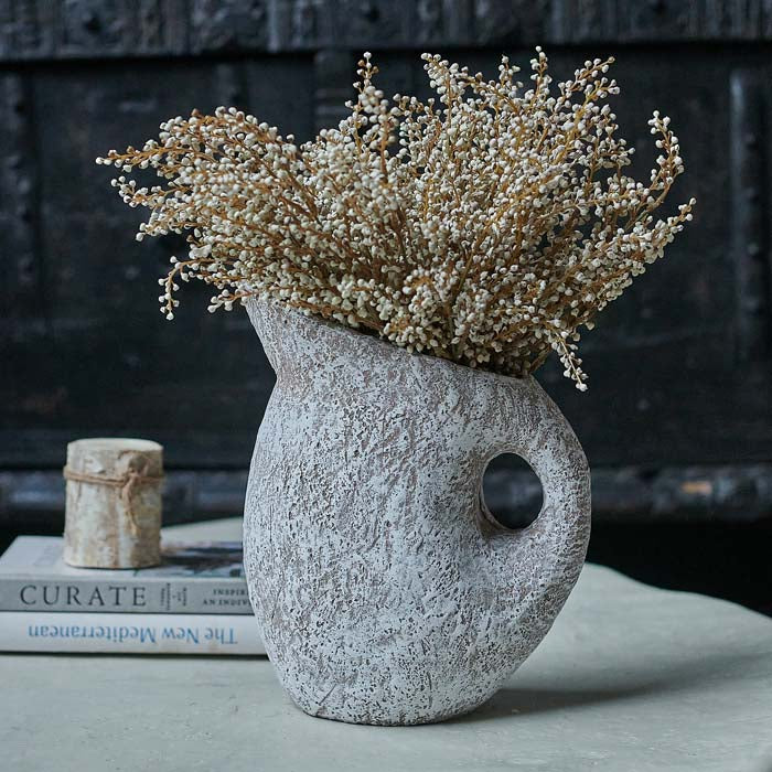 Textured white vase in a jug shape filled with cream flower stems