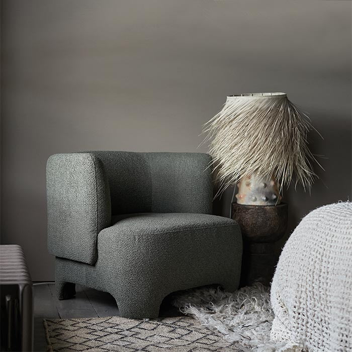 A green armchair and cream lamp on a warm grey paint backdrop
