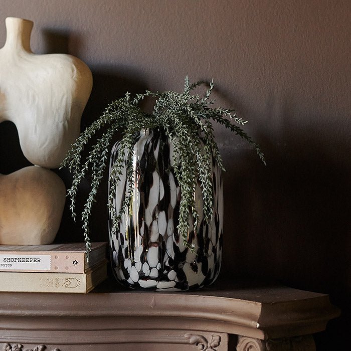 Red and white marbled glass vase filled with green spiky foliage sat on a mantle
