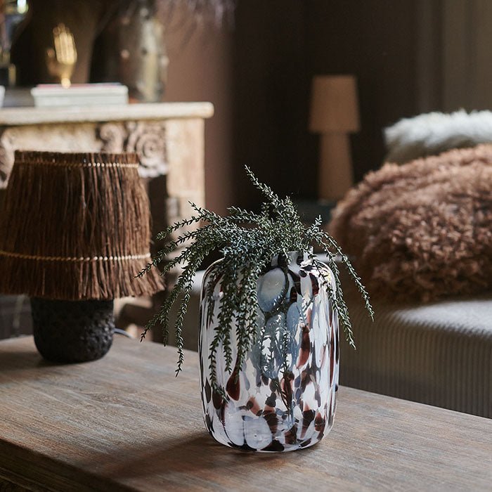 Red and white marbled glass vase filled with two stems of artificial green foliage sat on a wooden table