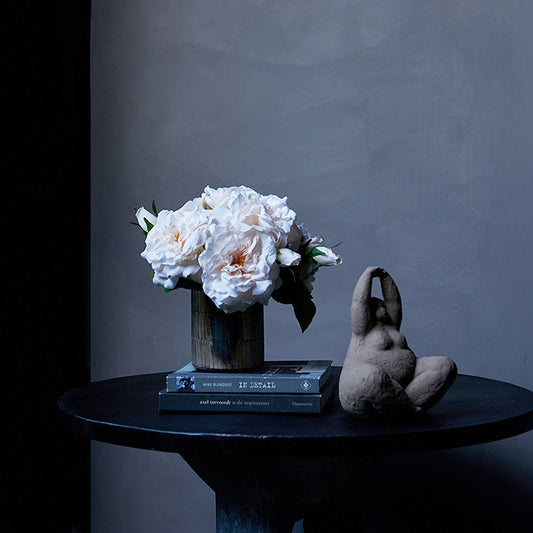 Six artificial garden roses in a vase, on a table.