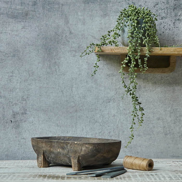 Trailing artificial green beaded plant in grey pot sat on a wooden shelf above a brown tray