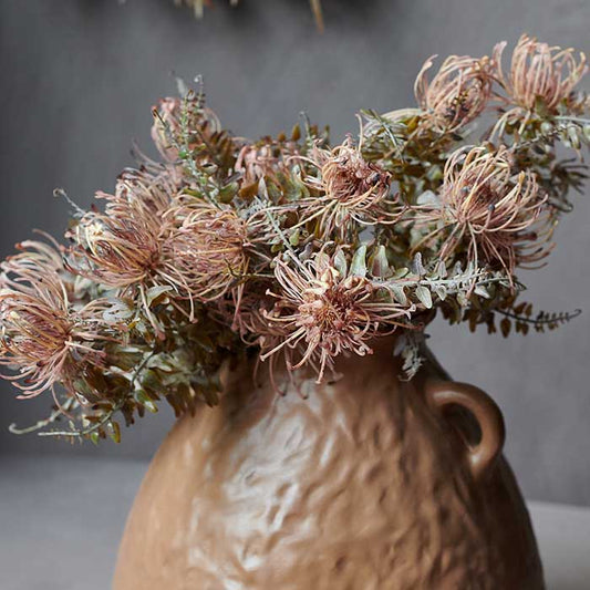 A large bunch of textural artificial foliage stems in a tall brown vase