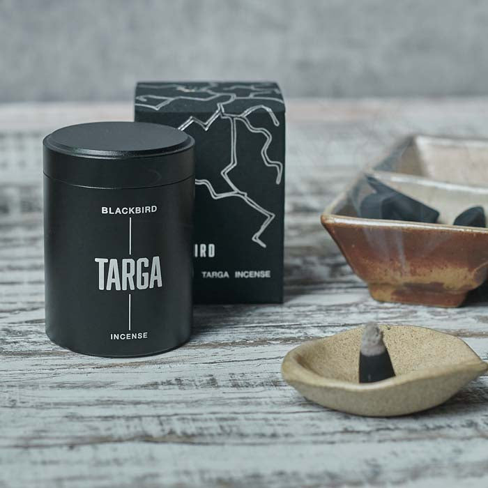 Burning incense cone in a small stoneware dish next to a black metal tin