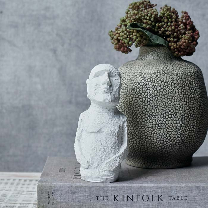 Small white figurine with hands on its stomach sat on a book 