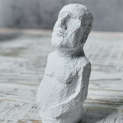 Small figurine in white with its arms resting on its stomach