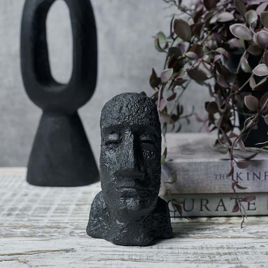 Black sculpture of a face and shoulders sat on a wooden table 
