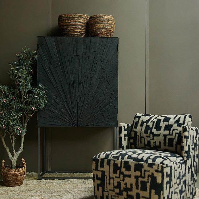 Tall black cabinet with wooden doors against a wall behind a patterned armchair