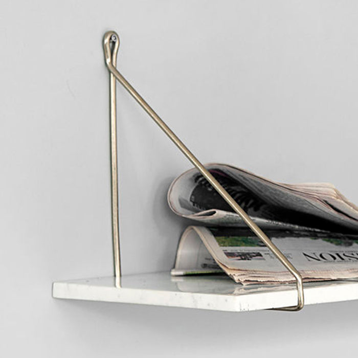 White marble shelf hanging from a gold triangular bracket with newspaper on