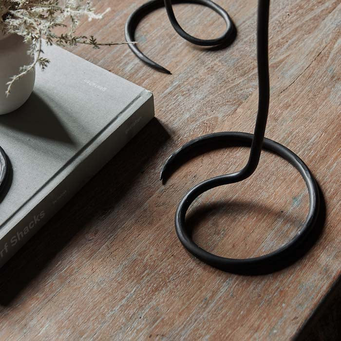 Thin metal wire candleholder on a swirl base sat on a dark wooden coffee tables