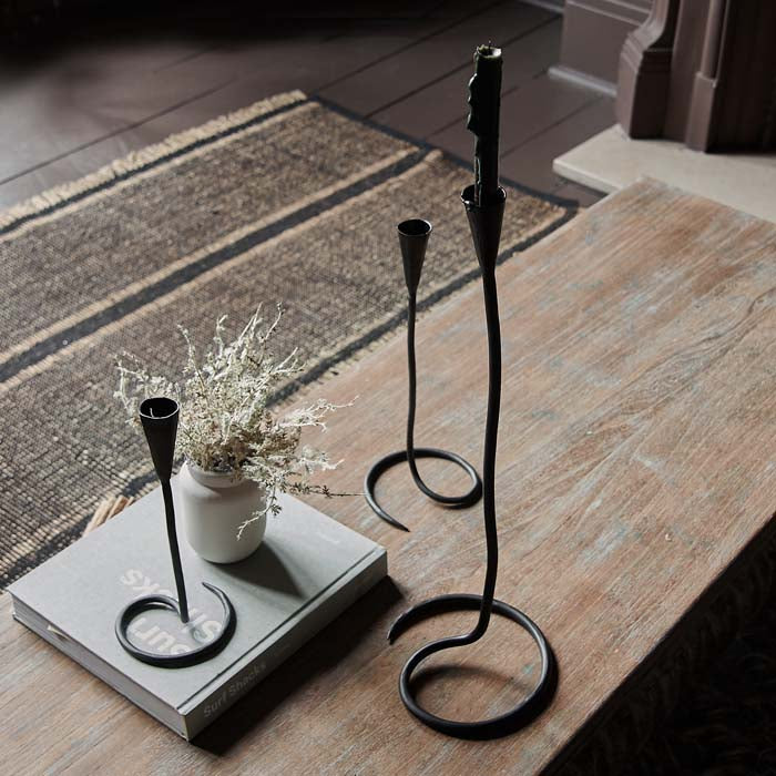 Three different sized black metal wire candleholders with a swirl base sat on a coffee table