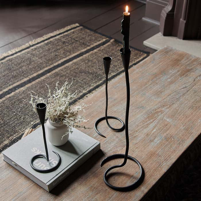 Three black metal swirl shaped candleholders in different sizes sat on a wooden coffee table