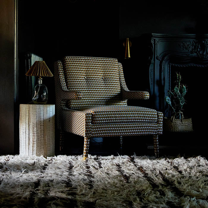 An upholstered orange and brown armchair in an abstract pattern with sculptural armrests and gold metal feet.