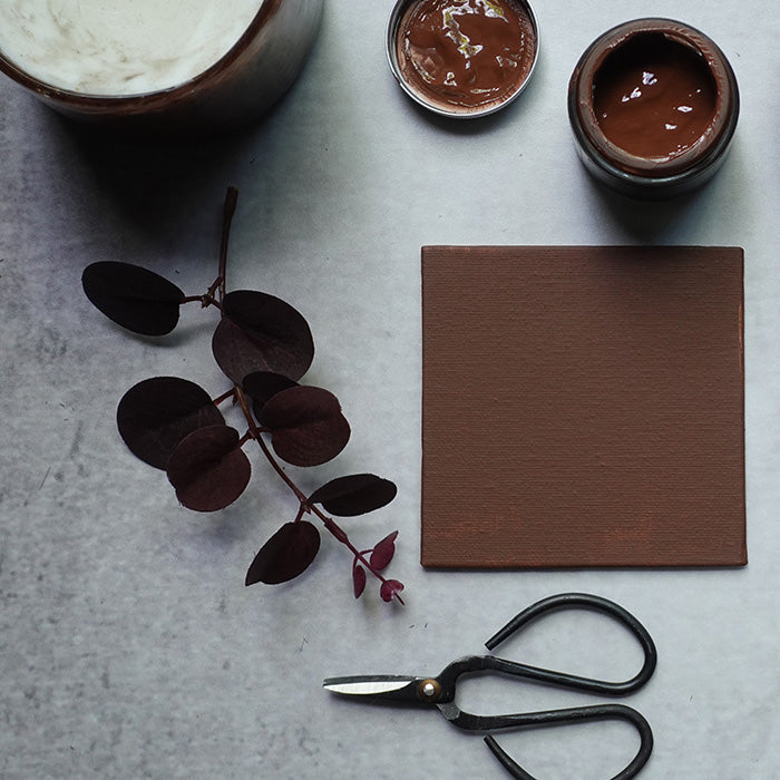 A brown painted tile with a red undertone next to an open sample pot