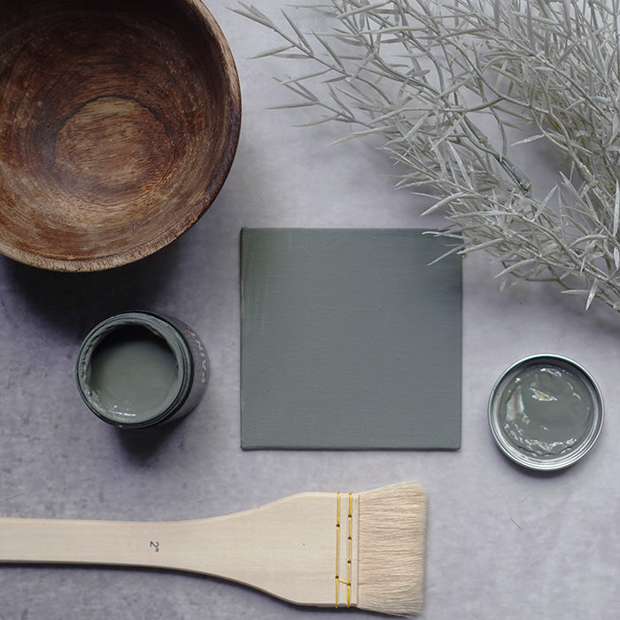 A rich green-grey painted tile next to an open sample pot and brush