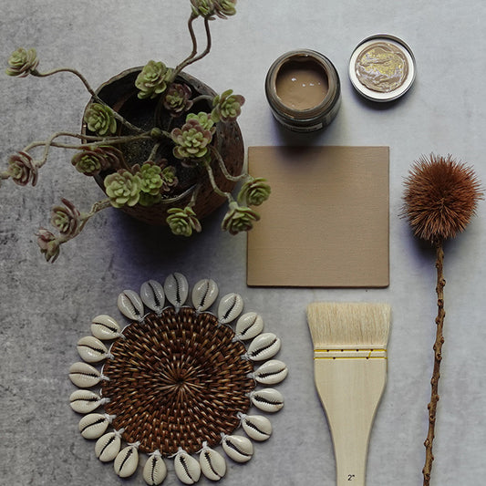 Sandy brown painted tile next to a faux plant and sample pot of paint. Wattle light coloured paint ideal for a living room.